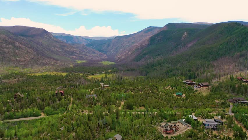 Drone shot over Grand Lake Colorado showing cabins, evergreen trees, hillside neighborhoods, and dramatic mountain terrain stretching across the high country valley