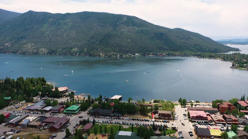 Drone shot over Grand Lake Colorado showing the waterfront marina, broad mountain lake, evergreen shoreline, and alpine ridges stretching across the high country horizon