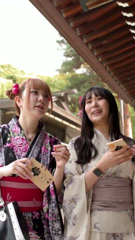 Two young women wearing traditional kimonos hold wooden prayer plaques at a Japanese Shinto shrine