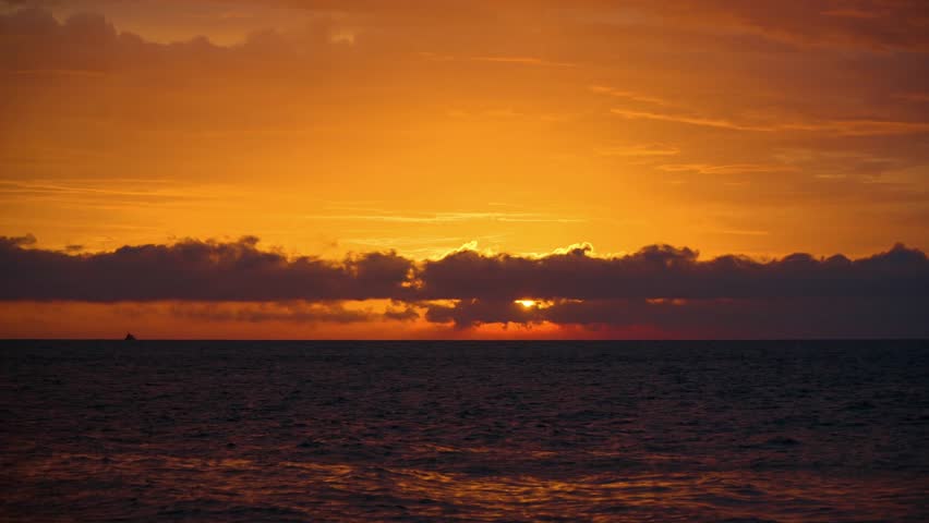 Beautiful Sunset Over Ocean with Sun Peeking Through Dark Clouds on the Horizon