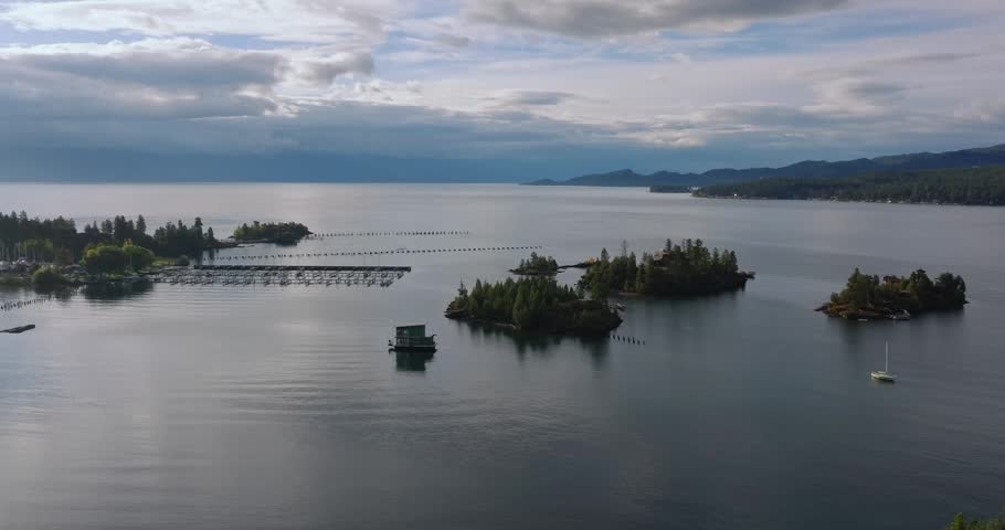 Small forested islands scattered across calm lake water around boat marina beneath a cloudy sky, Flathead Lake Montana USA
