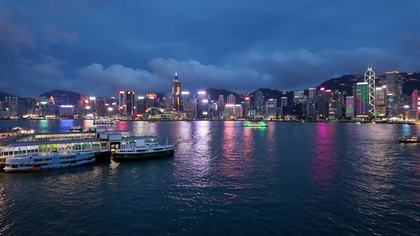Hong Kong, China: Cinematic panoramic footage of a ferry that crosses the Victoria harbor  between Kowloon Tsim Sha Tsui and Hong Kong island Central at night with a dramatic cloudy sky 