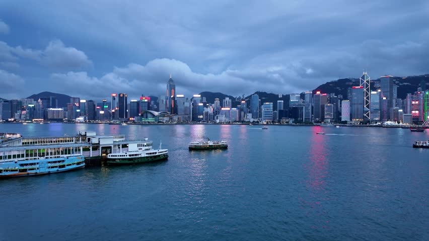 Hong Kong, China: Cinematic panoramic footage of a ferry that crosses the Victoria harbor  between Kowloon Tsim Sha Tsui and Hong Kong island Central at night with a dramatic cloudy sky 
