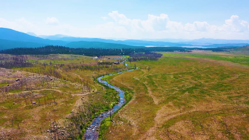 Aerial footage of Rocky Mountain National Park near Grand Lake Colorado capturing Kawuneeche Valley a curving stream broad grasslands rustic crossings and distant blue mountain ridges