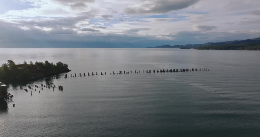 Wide open lake water with dock posts stretching toward distant horizon beneath layered clouds, Flathead Lake Montana USA