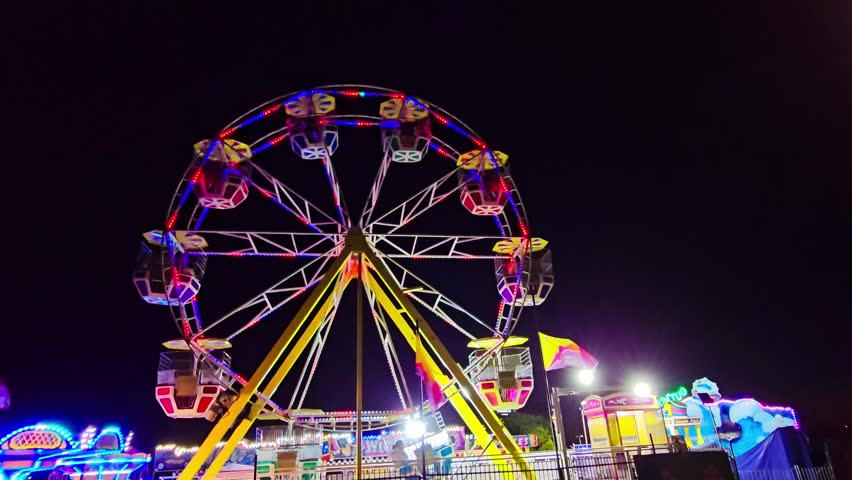 Colorful Ferris Wheel Rotating at Night in a Vibrant Amusement Park with Neon Lights