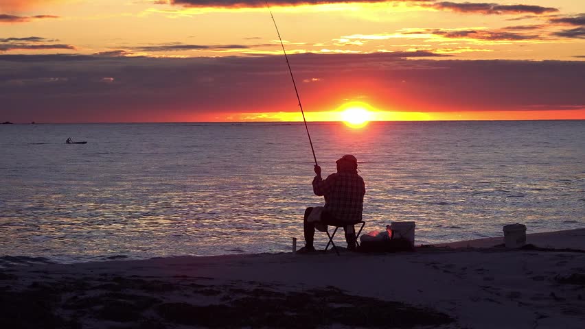 Silhouette of a Man Fishing on a Pier at Sunset with Vibrant Golden Sun Reflecting on Calm Ocean Water