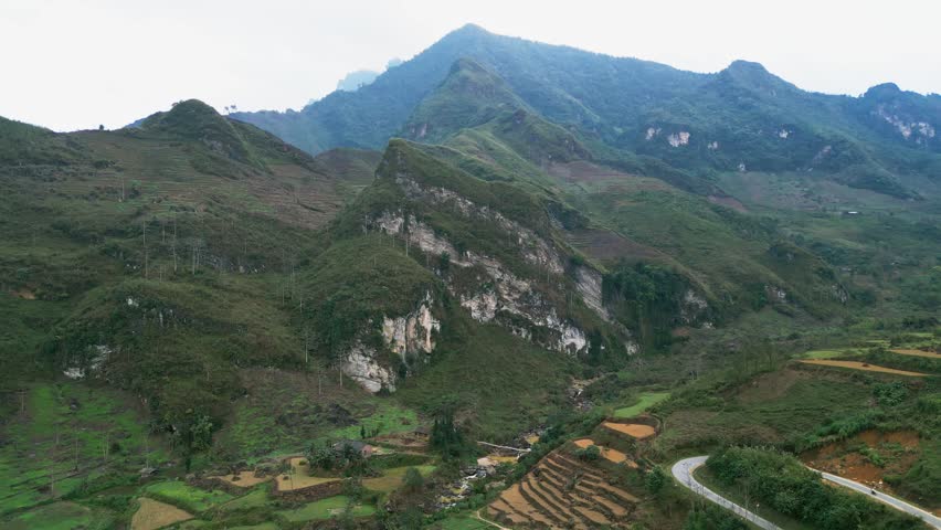 Aerial drone footage of terraced farmland in a mountain valley with limestone cliffs and a small stream flowing through green hills in a scenic highland landscape in northern Vietnam