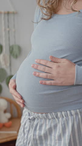 Pregnant woman cradles belly with hands in a softly lit studio with hanging mobile visible; maternal bonding tenderness.
