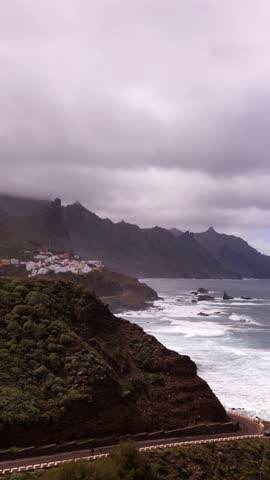 Dramatic panoramic view of Anaga coastline with mountain cliffs, white village, winding road and Atlantic ocean waves in Tenerife. Ideal for travel, tourism and nature projects