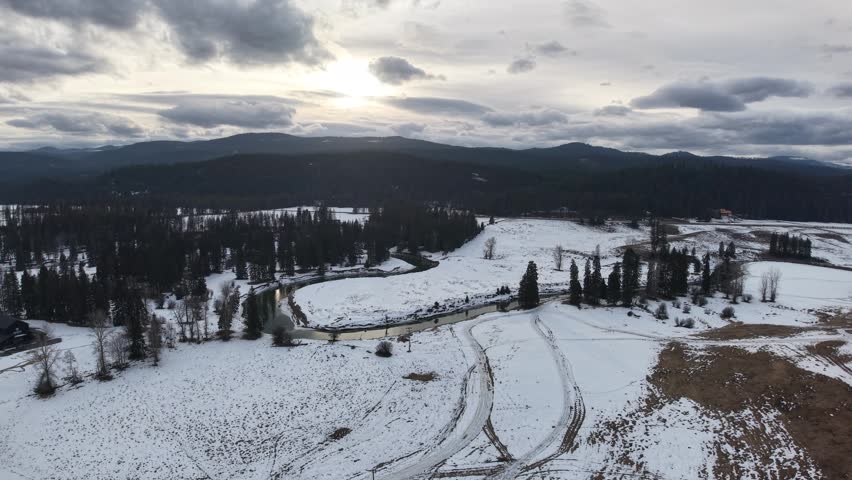 Aerial view of a snowy landscape with winding dirt roads and scattered pine trees under cloudy skies in Montana