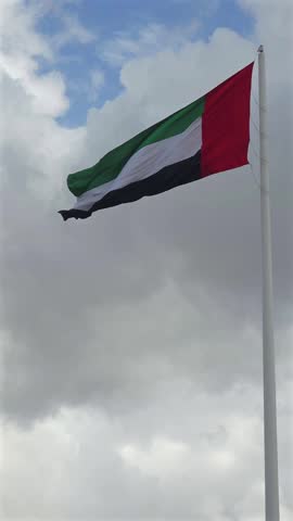The national flag of the UAE waves over Sharjah during a cloudy day.