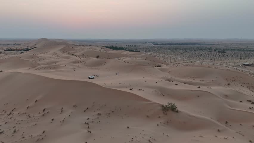 High angle aerial shot of vast desert sand dunes during twilight. A white 4x4 offroad vehicle is parked among the dunes, perfect for travel and adventure concepts.