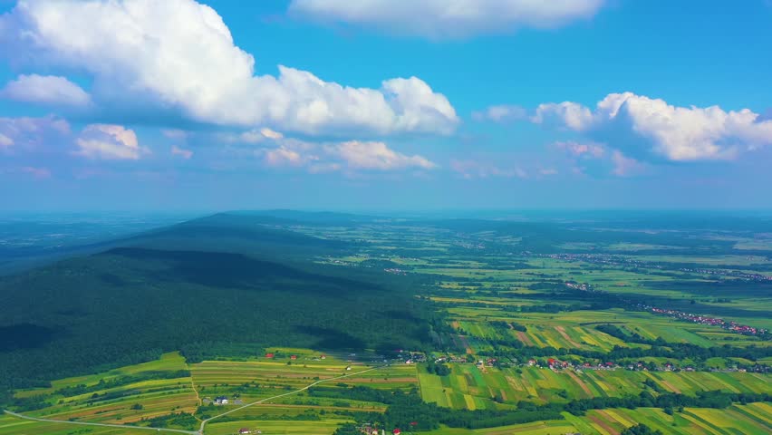 Aerial landscape over beautiful green farmland fields and mountain forest on sunny summer day
