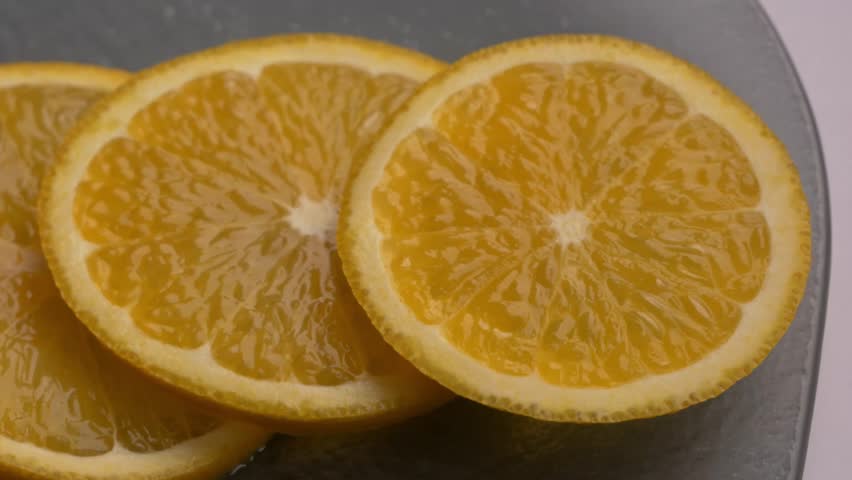 Slices of fresh orange displayed on a gray plate, highlighting the juicy texture and bright colors of the fruit. Fresh orange sliced