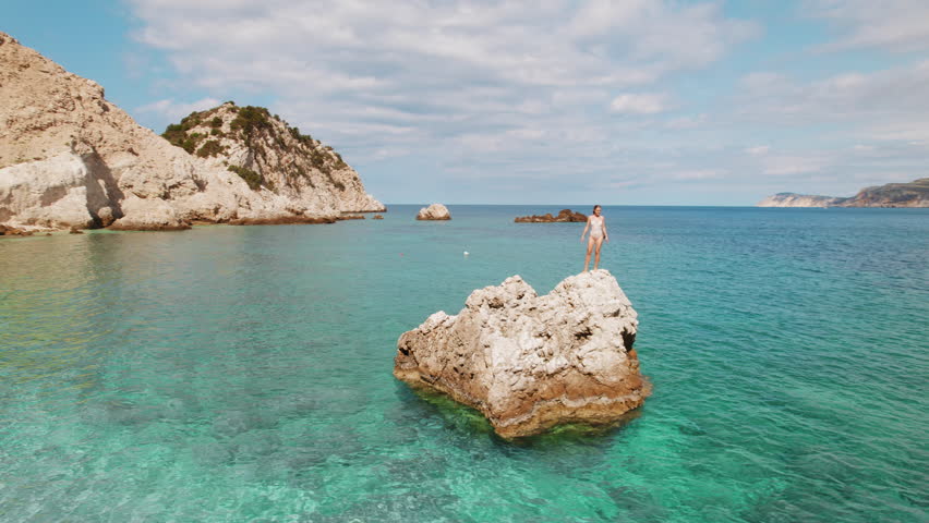 Woman enjoying on a rock above turquoise sea on a sunny summer day in Greece