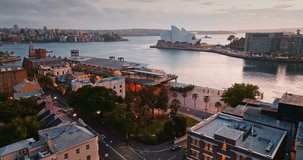 Sydney Opera House and Circular Quay waterfront at dramatic cloudy sunset dusk, ferries crossing the harbor and city skyline reflected in rippling water, iconic urban landmark. Aerial drone flight - Powered by Shutterstock - Get 15% off with code: PIKWIZARD15