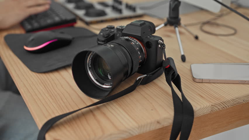Man photographer typing with hands on keyboard beside camera and microphone in studio, red cup on desk; concentration creativity.