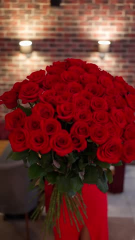 A large bouquet of red roses held by a woman in an elegant dress. A romantic gift concept.