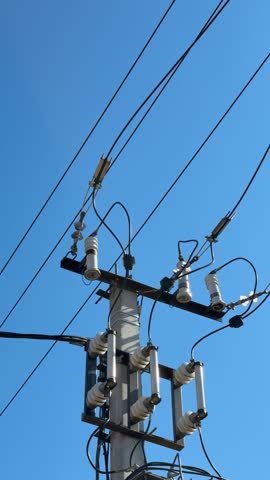 Electric pole transformer under clear sky, concrete pillar supporting high voltage wires, porcelain insulators, metal brackets.