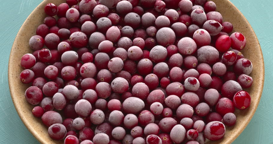 Raw, frozen cranberries on a plate. Table spin, blue background.