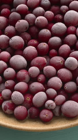 Raw, frozen cranberries on a plate. Blue background, vertical video.