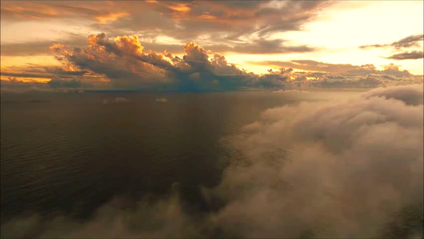 A serene aerial view of a calm ocean surface partially obscured by thick clouds at golden sunset