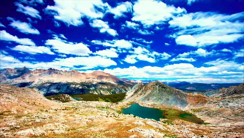 A scenic view of a rocky mountain landscape under a bright blue sky filled with white clouds.