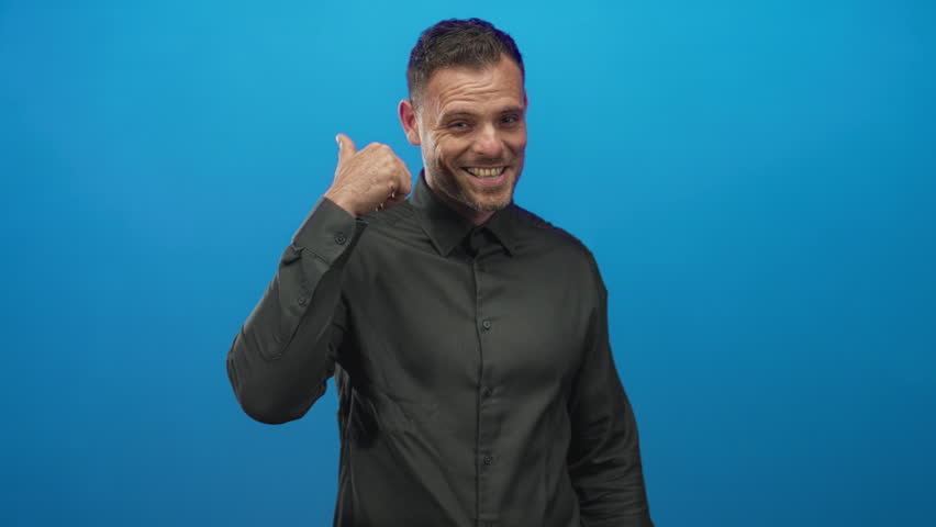 Man smiling and giving a thumbs up with visible thumb in studio with blue backdrop; confidence endorsement.