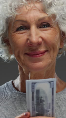 Portrait: Happy senior woman with grey hair counting USD banknotes. Rich old lady getting rich with jackpot. Face of mature female person holding cash money paper dollars. Wealth retirement concept