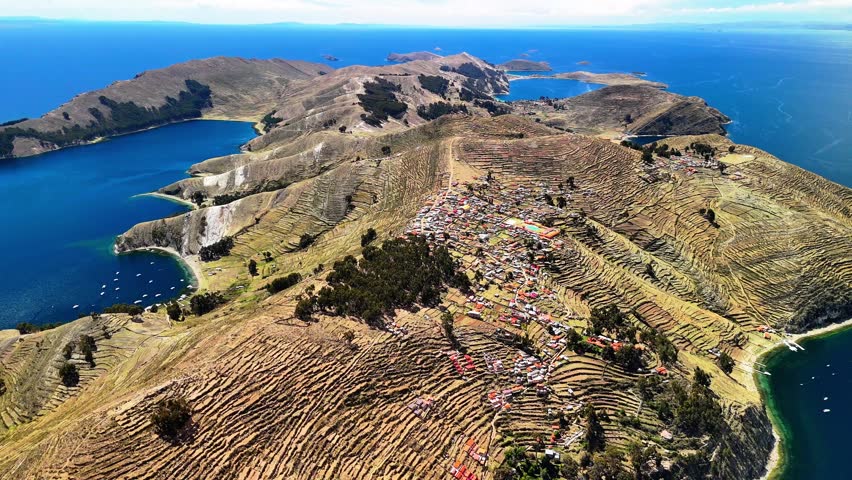 Aerial drone view of the Island of the Sun on Lake Titicaca in Bolivia. Isla del Sol in the Andes Mountains. A landscape with a small village surrounded by deep blue water.	
