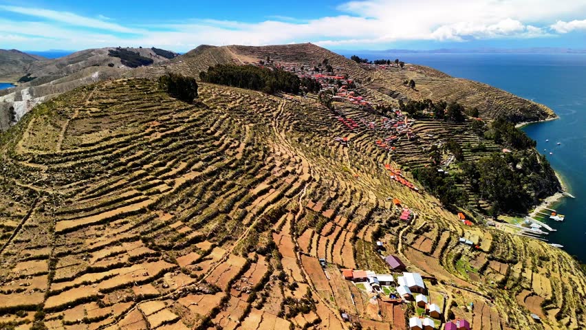 Aerial drone view of the Island of the Sun on Lake Titicaca in Bolivia. Isla del Sol in the Andes Mountains. A landscape with a small village surrounded by deep blue water.	