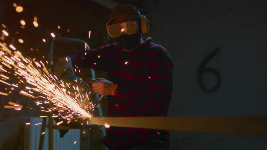Welder at work in industry, cutting - slow motion. Lots of sparks in factory. Man cuts metal with a angle grinder. Male at a construction site cuts off a piece of metal, fiery sparks and particles fly