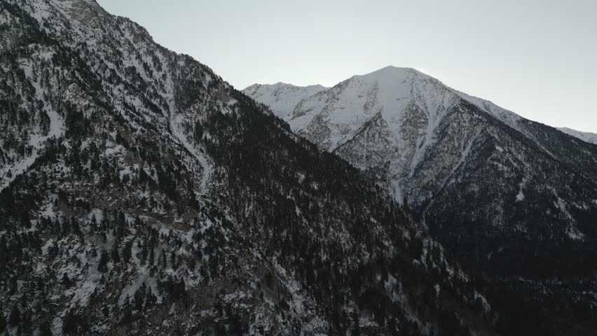 Drone aerial shot of a mountain landscape with evergeen pine trees standing out against snow covered terrain
