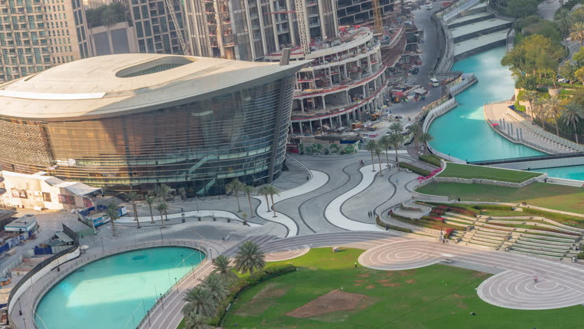 Dubai Opera located in Downtown is the radiant center of culture and arts. Aerial evening top view showing the artificial lake and park with palm trees in time-lapse.