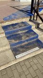 Worn blue anti slip stairs outdoors, scuffed textured coating on concrete treads, metal nosing at base, rusted railing casting long. - Powered by Shutterstock - Get 15% off with code: PIKWIZARD15