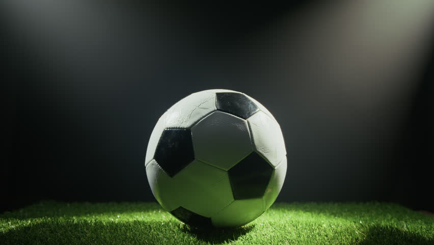 Lights flashing illuminate a football ball in the stadium at night on the meadow