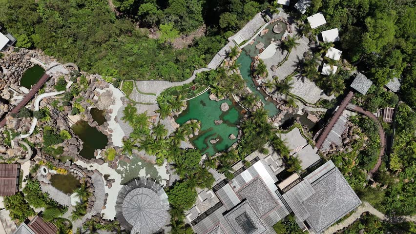 Static aerial drone shot of tropical resort with lagoon pools, palm trees and pathways surrounded by lush greenery. Top view composition ideal for travel, luxury and resort concepts.