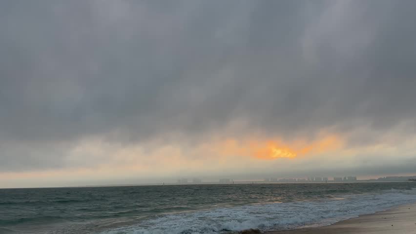 4K horizontal wide shot of a stunning red sunset glow over the ocean, with waves in the foreground and a distant city skyline in Sanya, Hainan.