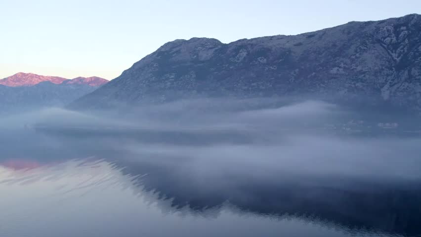 Breathtaking UHD cinematic shot of tranquil fog drifting over a serene lake with mountains in the background at dawn. Ideal for nature documentaries and relaxation content.