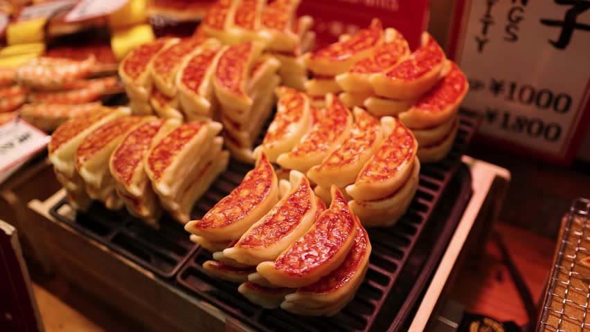 Close-up handheld shot of golden brown gyoza and grilled shrimp skewers at Dotonbori market