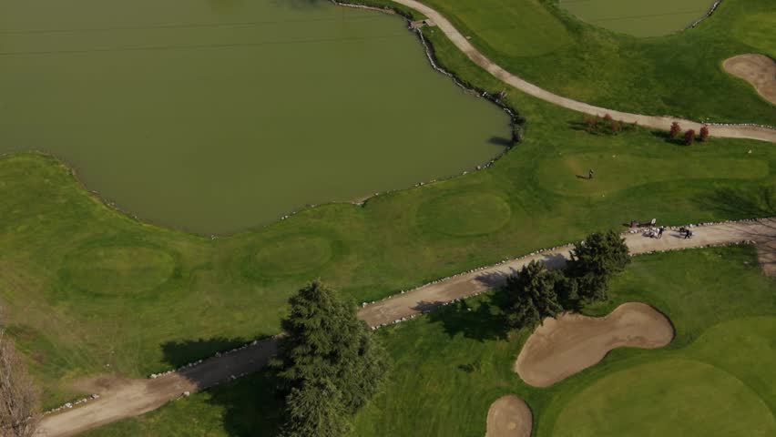 Aerial drone view of golfer hitting ball on green golf course, capturing motion, technique, and landscape from above in natural daylight.