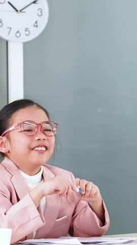 Young Asian girl wearing glasses and pink blazer smiles and writes during a mock interview