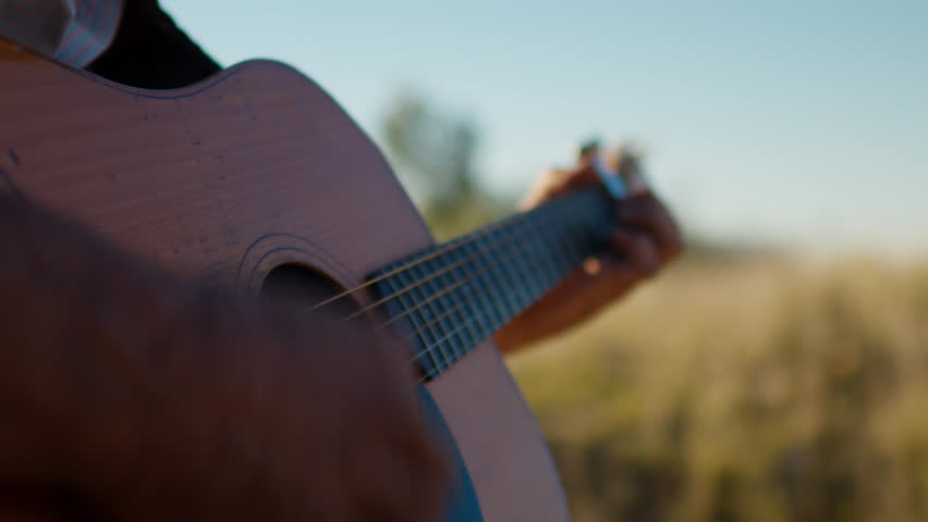 Close up, A musician strumming on an acoustic guitar, moving his fingers onto the different cords and strings.