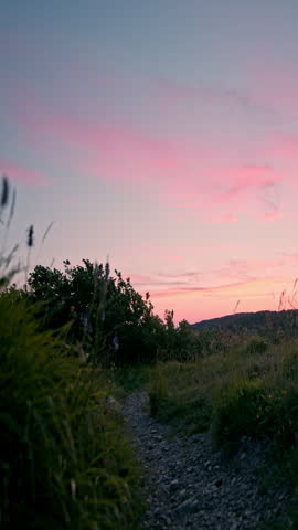 Peaceful sunset over grassy hill with path and pink sky
