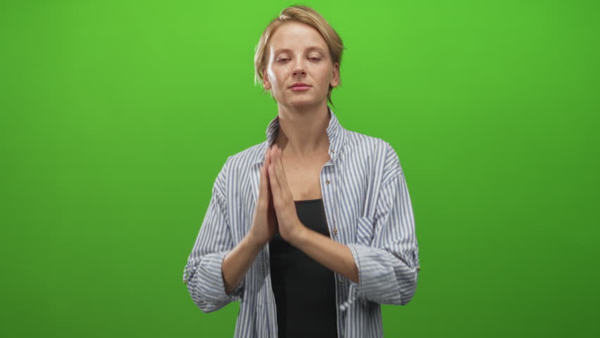 Woman with hands pressed to cheek in sleeping gesture wearing striped shirt on green studio set; serenity.