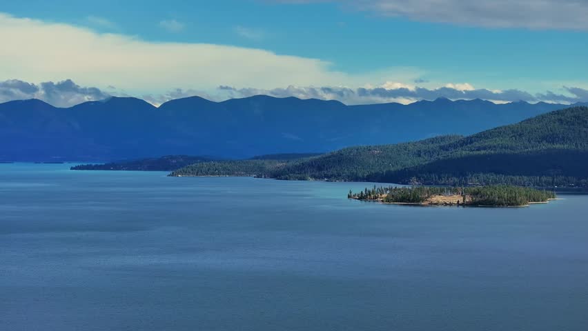 Distant mountain range rising beyond vast calm lake water with gentle shoreline contours and expansive blue horizon, Flathead Lake Montana USA