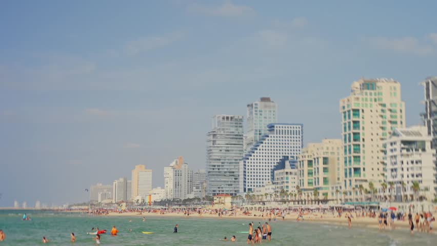 Local people and tourists enjoy summer day at the beach in Tel Aviv Israel. Vacation holiday swimming and bathing by Mediterranean Sea water. Hotels along the coast promenade. Hot weather day of fun