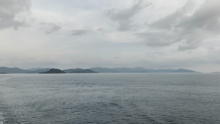 Calm waters meet rugged mountains under a somber sky.