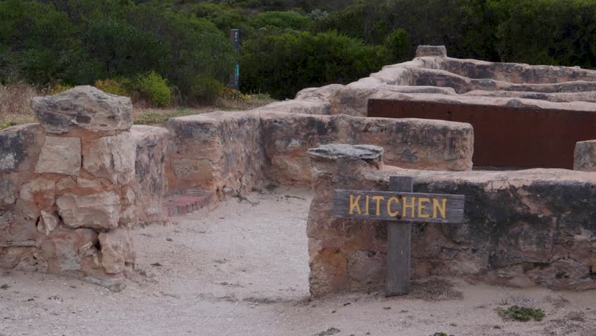 A weathered sign marks the kitchen area of an ancient stone structure surrounded by lush greenery. Ideal for historical or educational content.